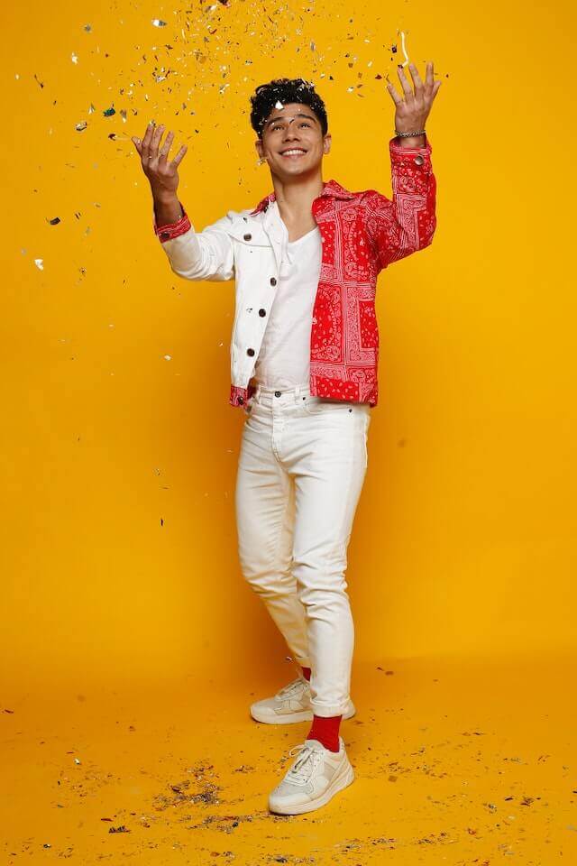 male model smiling and throwing glitters in the air with orange background
